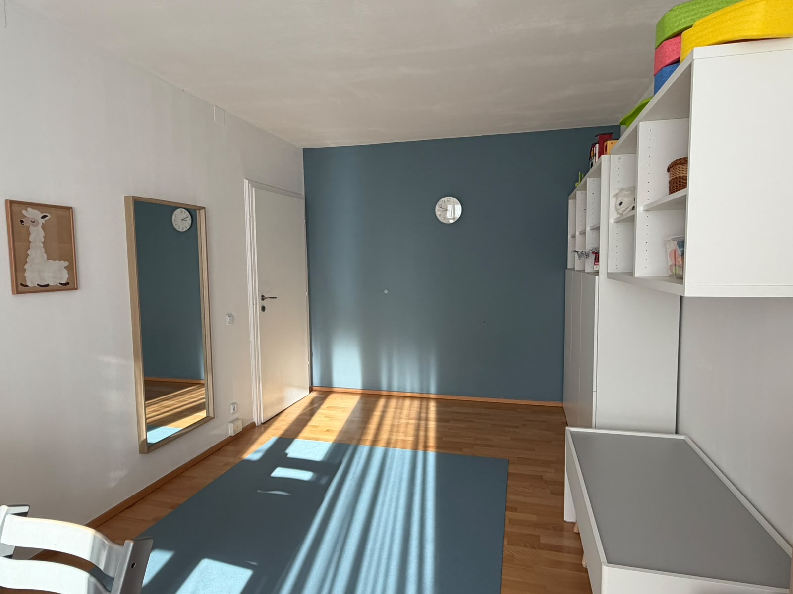 Freie Spielfläche mit blauer Matte, Wandspiegel und blauer Akzentwand im Therapieraum